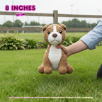 A crocheted dog toy held by a person's hand outdoors on a grassy lawn, with text overlays indicating 8 inches (20 cm) size. The toy is brown and white with black eyes and a stitched nose.