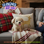 A crocheted plush puppy toy sits on a gray sofa wrapped in a cream knit blanket with red stripes, alongside a plaid pillow, a deer-print pillow, and a person's arm. Text overlays indicate 10 inches (25 cm) size, with a note stating the product is 100% handmade.