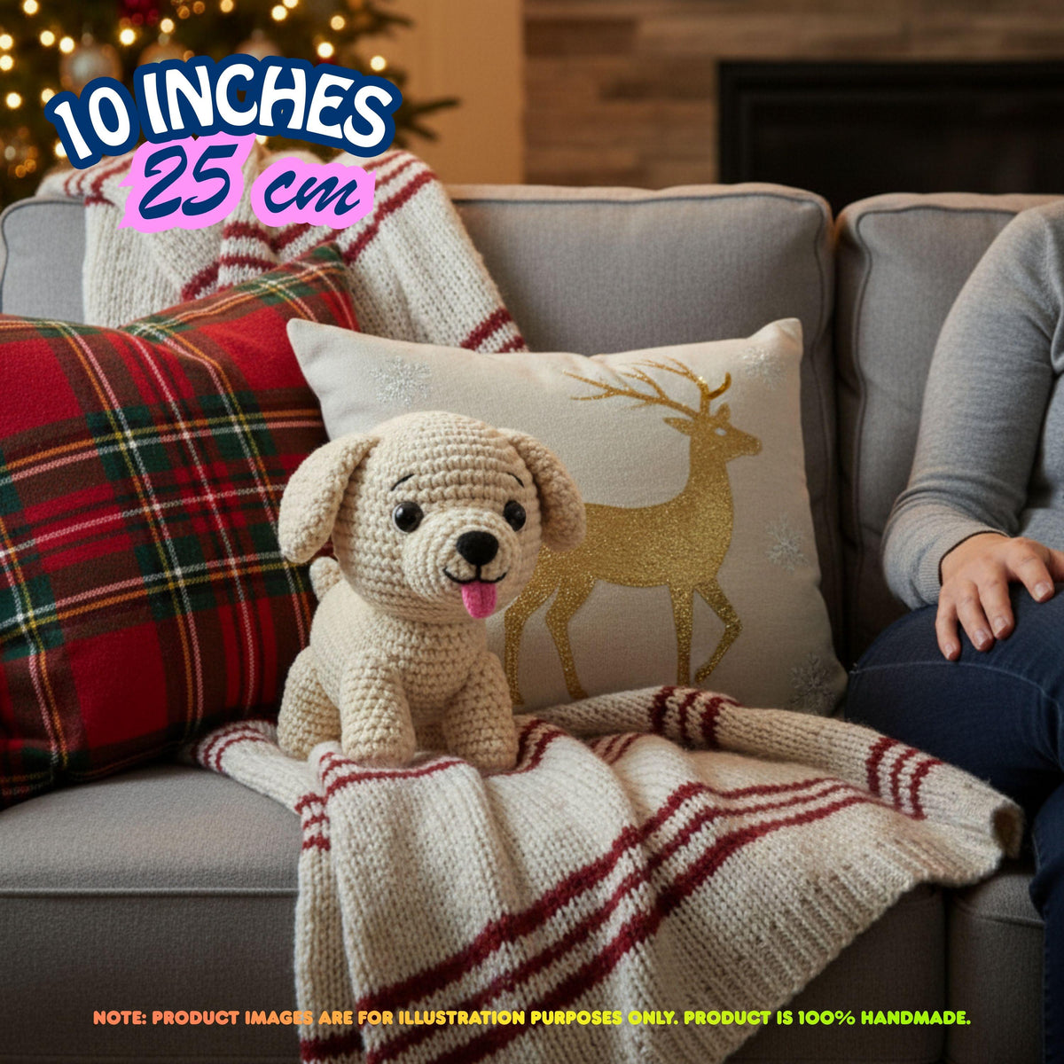 A crocheted plush puppy toy sits on a gray sofa wrapped in a cream knit blanket with red stripes, alongside a plaid pillow, a deer-print pillow, and a person's arm. Text overlays indicate 10 inches (25 cm) size, with a note stating the product is 100% handmade.