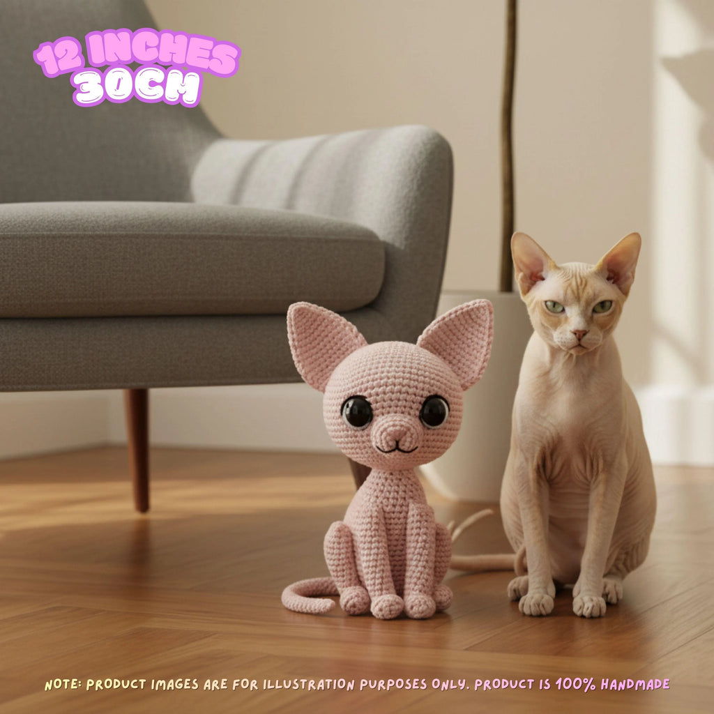 A crocheted cat toy sits on a wooden floor next to a real cat in a living room setting, with a gray armchair in the background and text overlays indicating the size and handmade nature of the product.