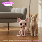 A crocheted cat toy sits on a wooden floor next to a real cat in a living room setting, with a gray armchair in the background and text overlays indicating the size and handmade nature of the product.