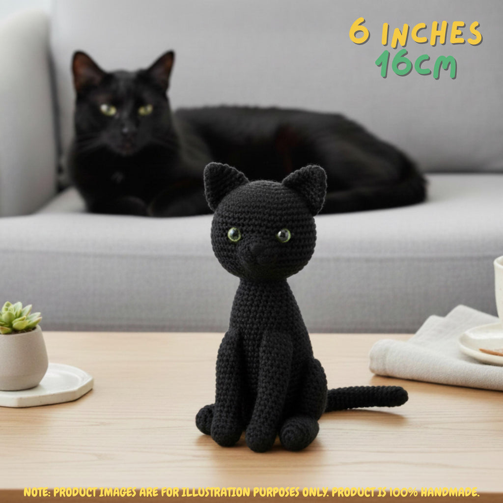A black crocheted amigurumi cat sits on a wooden table in the foreground, with a real black cat resting on a light gray sofa in the background. Text in the top right reads '6 INCHES 16CM', and a note at the bottom says the product images are for illustration purposes only.