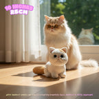 A small crocheted cat toy sits on a wooden floor in front of a fluffy cream-colored cat in a sunlit room. The image includes text overlays indicating the product size is 10 inches (25 cm) and a note that product images are for illustration purposes only.