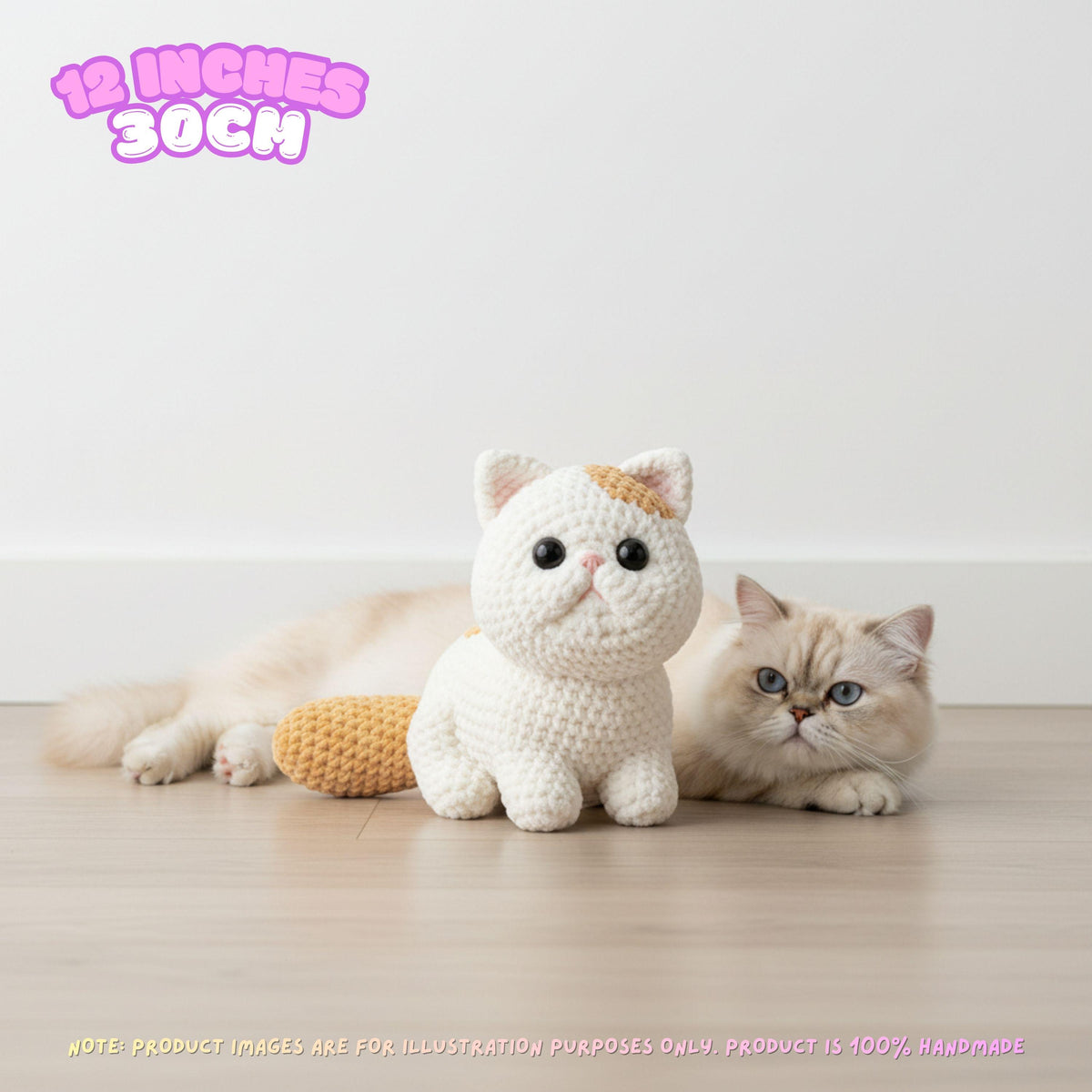 A crocheted cat plush toy in cream and orange-yellow sits on a light wood floor next to a real fluffy cream cat in a bright room. Pink text in the top left says '12 INCHES 30CM'.