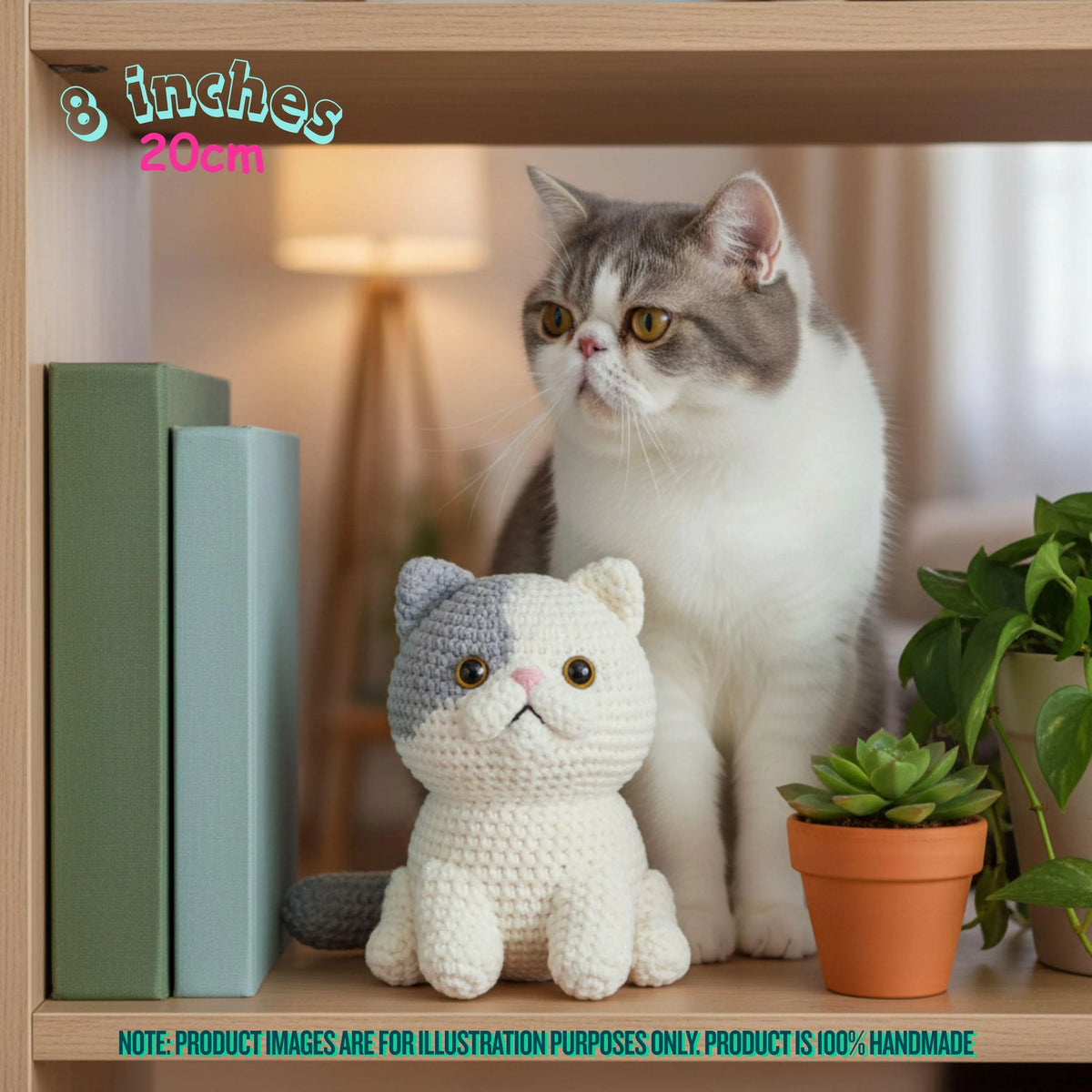 A small crocheted cat toy sits on a wooden shelf beside a real cat in a home interior, with books, a potted plant, and a warm lamp in the background. Text in the image notes the product is 8 inches / 20 cm and says the product image is for illustration purposes only.