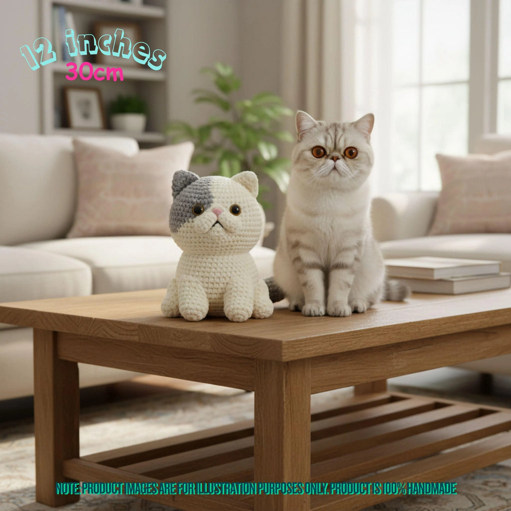 A crocheted plush cat toy sits on a wooden coffee table next to a real cat in a bright living room. Text in the top left reads '12 inches 30cm', and a note at the bottom says product images are for illustration purposes only.