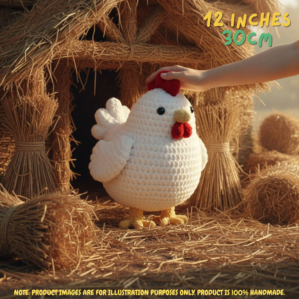 Crocheted white chicken plush toy with red comb and wattle, standing in front of a straw hay bale. A human hand is touching the top of the chicken's head.