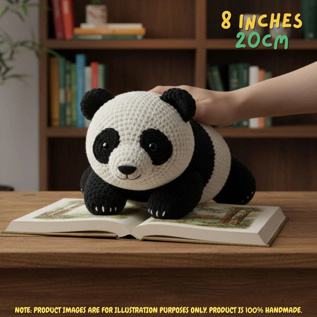 Hand gently resting on top of a handmade giant panda bear crochet amigurumi plush doll lying on an open book on a wooden table in front of a bookshelf, with text reading 8 INCHES 20cm.