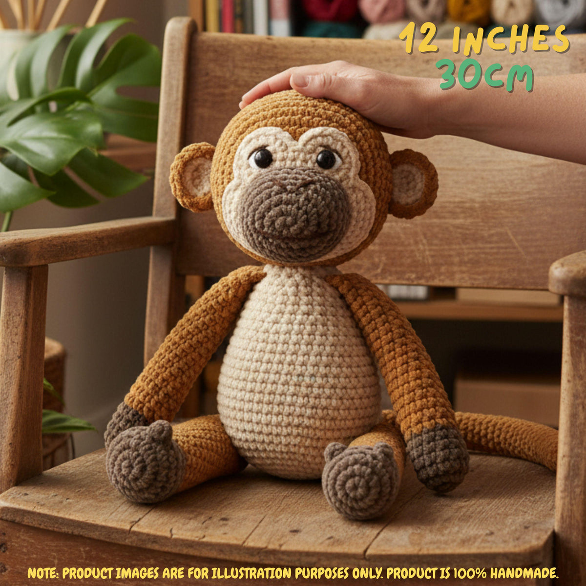 A crocheted plush monkey toy sitting on a wooden chair, with a human hand resting on its head. The toy has a cream-colored belly and inner ears, medium brown arms and legs, and a darker brown snout, ears, and feet.