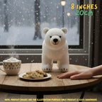 A crocheted white polar bear toy sits on a wooden table in front of a snowy window, with a mug of hot cocoa, a plate of cookies, and a hand reaching toward it. Text in the top right reads '8 INCHES 20CM', and a note at the bottom says product images are for illustration purposes only.