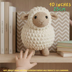 A crocheted plush sheep toy with a cream-colored textured body, tan face and legs, and small black eyes, displayed on a wooden shelf next to books. A human hand is touching the bottom of the toy, and text overlays indicate its size as 10 inches (25 cm) with a note at the bottom stating the product image is for illustration purposes only.