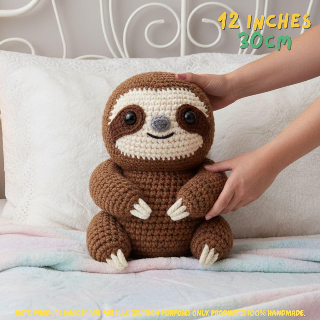 Handmade brown crochet sloth amigurumi doll with white claws sitting on a bed with a hand resting on its arm, featuring "12 INCHES / 30CM" text overlay.