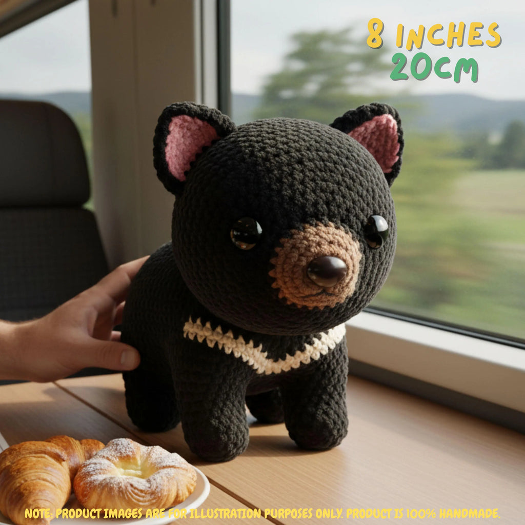 Handmade Tasmanian Devil crochet amigurumi plush doll with cream chest stripes sitting on a wooden table, with a hand holding it next to fresh pastries by a train window, with text indicating 8 inches 20 cm size.