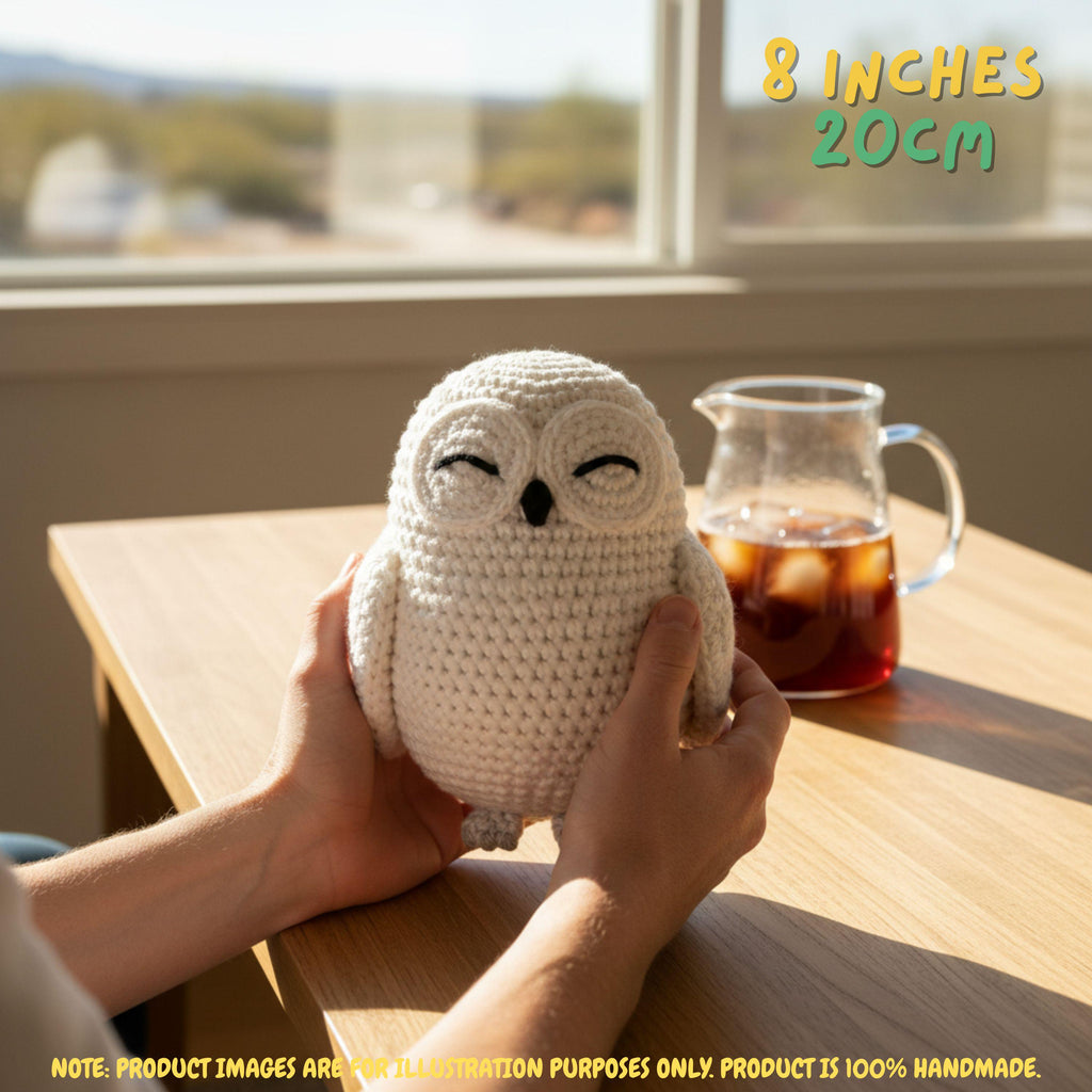 A crocheted owl plush toy being held by two hands on a wooden table near a window, with a glass pitcher of iced tea in the background. Text overlays indicate the size is 8 inches (20 cm) and note that the product image is for illustration purposes only.
