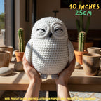 A crocheted owl plush toy being held in two hands, with the text '10 INCHES 25CM' in the top right and a note at the bottom. The owl is off-white with black embroidered eyes and a small black beak.
