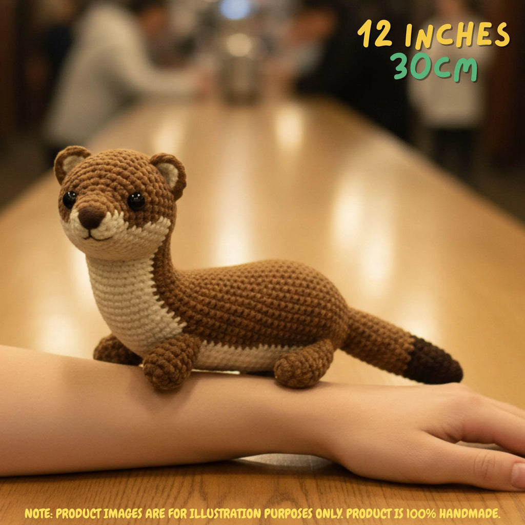 Handmade Stoat crochet amigurumi plush doll in brown and cream with a dark-tipped tail held in a hand on a wooden table, with text indicating 12 inches 30 cm size.
