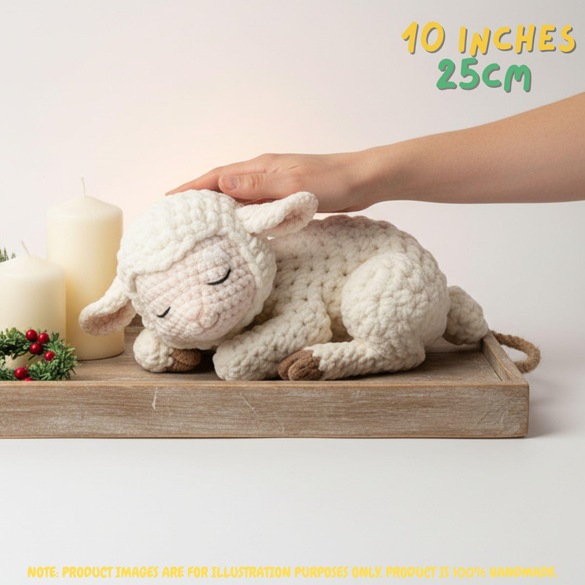 A crocheted sleeping sheep plush toy in cream white yarn, resting on a wooden tray with two white candles and a hand gently touching its head. Text overlays indicate '10 INCHES 25CM' and note the product is 100% handmade.