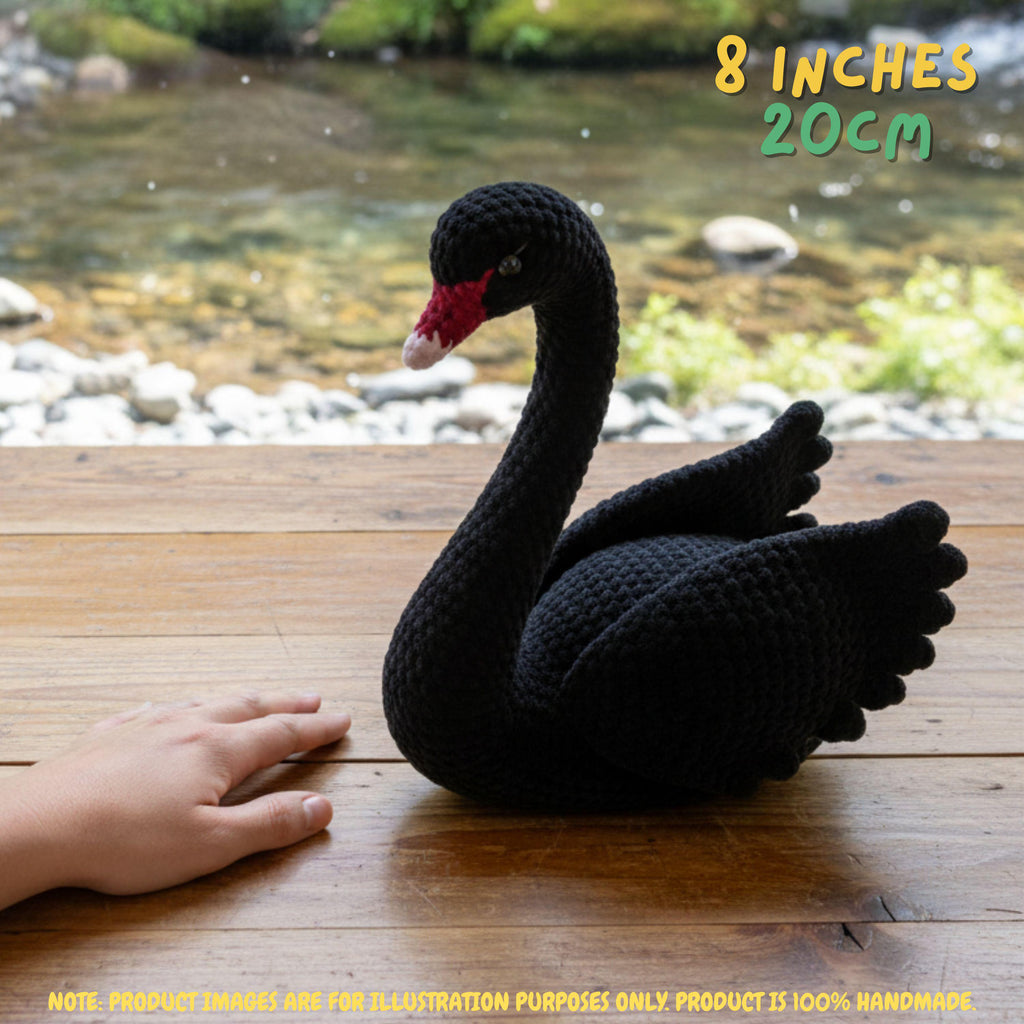 Handmade black swan crochet amigurumi doll with a graceful curved neck and red beak resting on a wooden deck by a stream, with "8 INCHES 20CM" text overlay.
