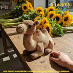 A crocheted camel toy sits on a rustic wooden table, with a person's hand reaching toward it. Bright sunflowers are arranged in the background, and text overlays indicate the size as 8 inches (20cm) with a note that the product images are for illustration purposes only since the product is 100% handmade.