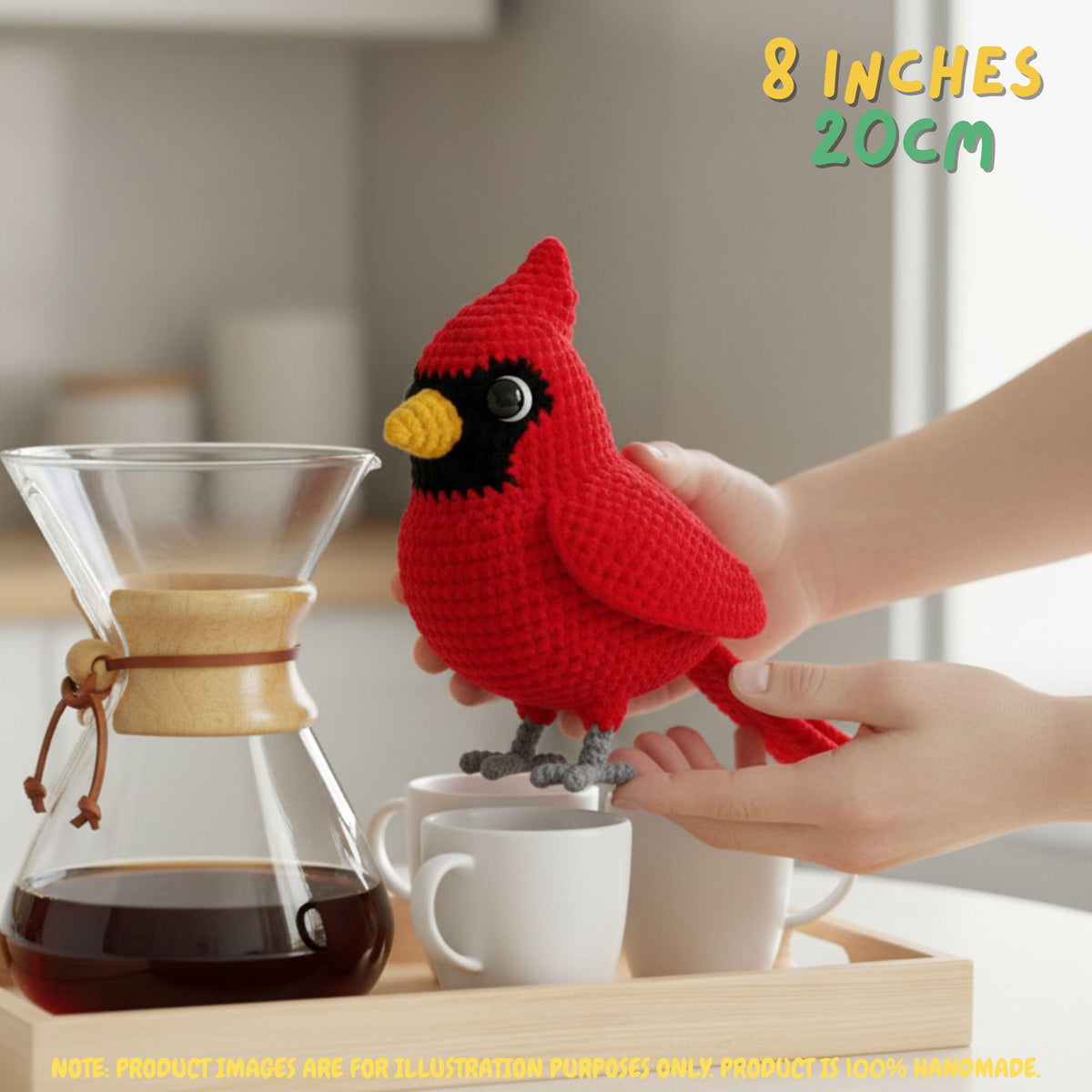 A red crocheted bird figurine with a yellow beak, black eye patch, and gray feet is being held by two hands over a coffee maker and two white cups. Text in the top right reads '8 INCHES 20CM'.