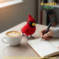 A red crocheted bird ornament stands on a wooden table beside a cup of latte art, an open notebook, and a hand holding a pen. Yellow text in the top right reads '6 INCHES 16CM', and a note at the bottom says product images are for illustration purposes only.