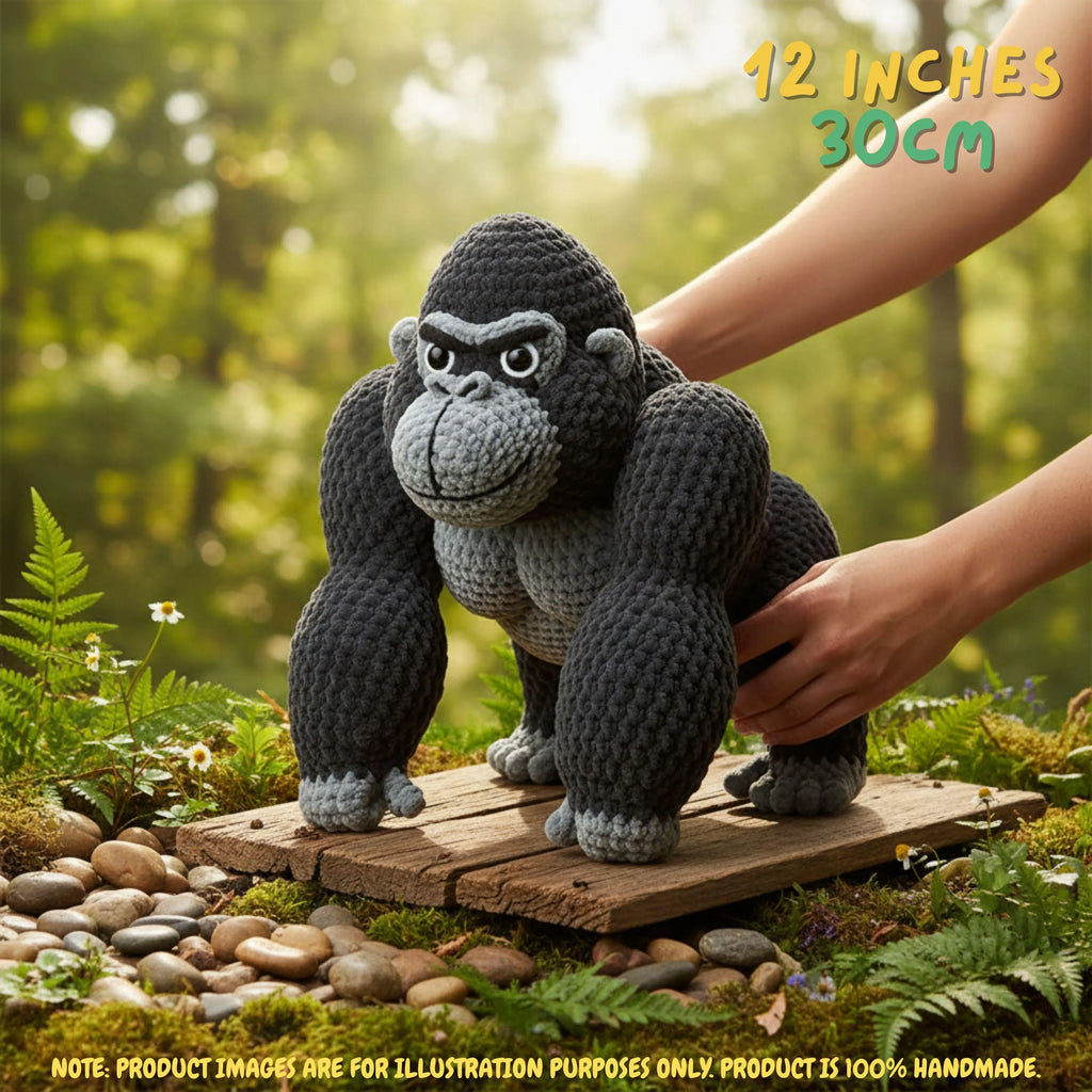 A crocheted gorilla toy standing on a small wooden platform outdoors, with human hands supporting it. The background is a blurred green forest setting, and text in the top right reads '12 INCHES 30CM'.