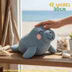 Handmade blue manatee crochet amigurumi doll with pink cheeks, featured with a "12 inches / 30 cm" size text overlay in a coastal room setting.