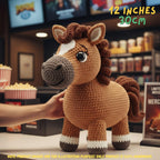 A crocheted horse toy being held by a hand in a movie theater lobby, with text overlay indicating its size is 12 inches (30 cm).