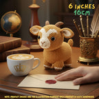 A crocheted plush goat toy sits on a wooden desk beside a cup of latte, an envelope with a red wax seal, and a hand reaching toward it. Text in the top right reads '6 INCHES 16CM', and a note at the bottom says the product images are for illustration purposes only because the product is 100% handmade.