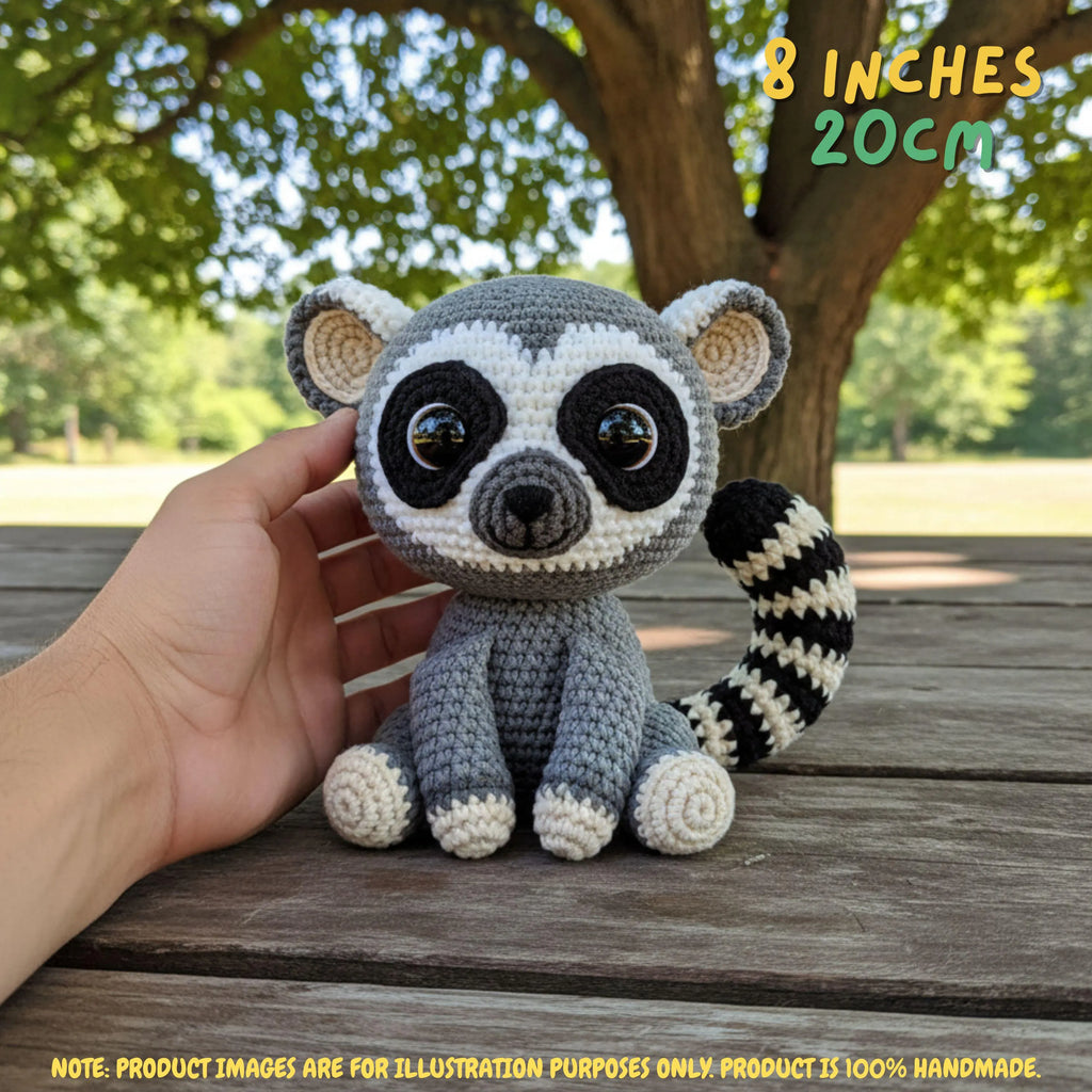 A crocheted raccoon toy being held by a human hand outdoors on a wooden bench, with trees in the background. Text in the top right says '8 INCHES 20CM', and a note at the bottom says product images are for illustration purposes only.