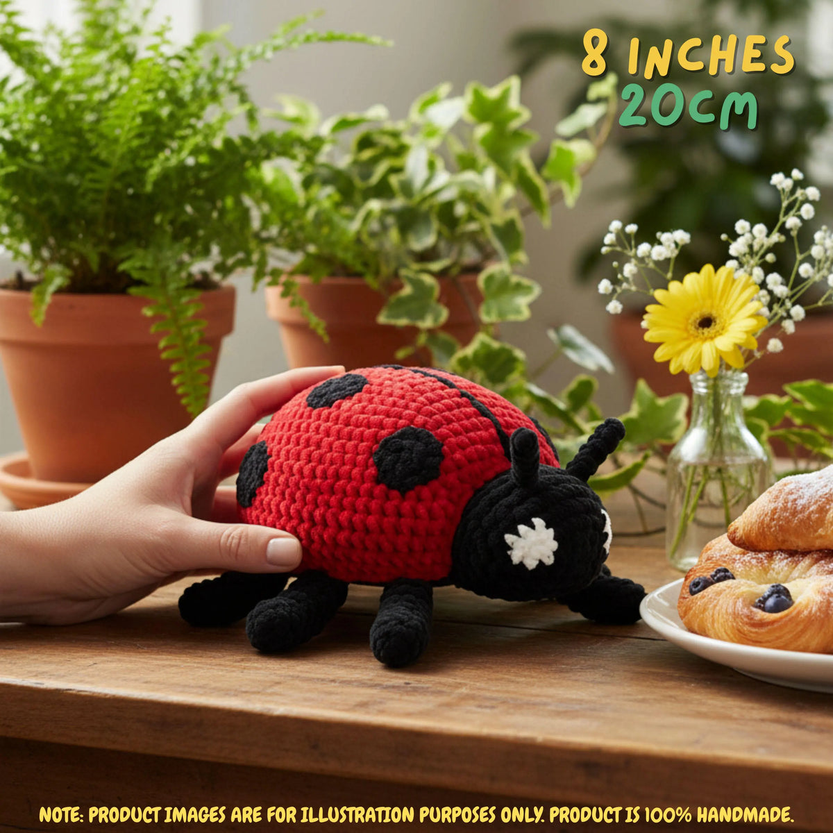 A crocheted ladybug toy being held by a hand on a wooden table, with potted plants, a small vase of flowers, and pastries in the background. Text in the top right reads '8 INCHES 20CM'.
