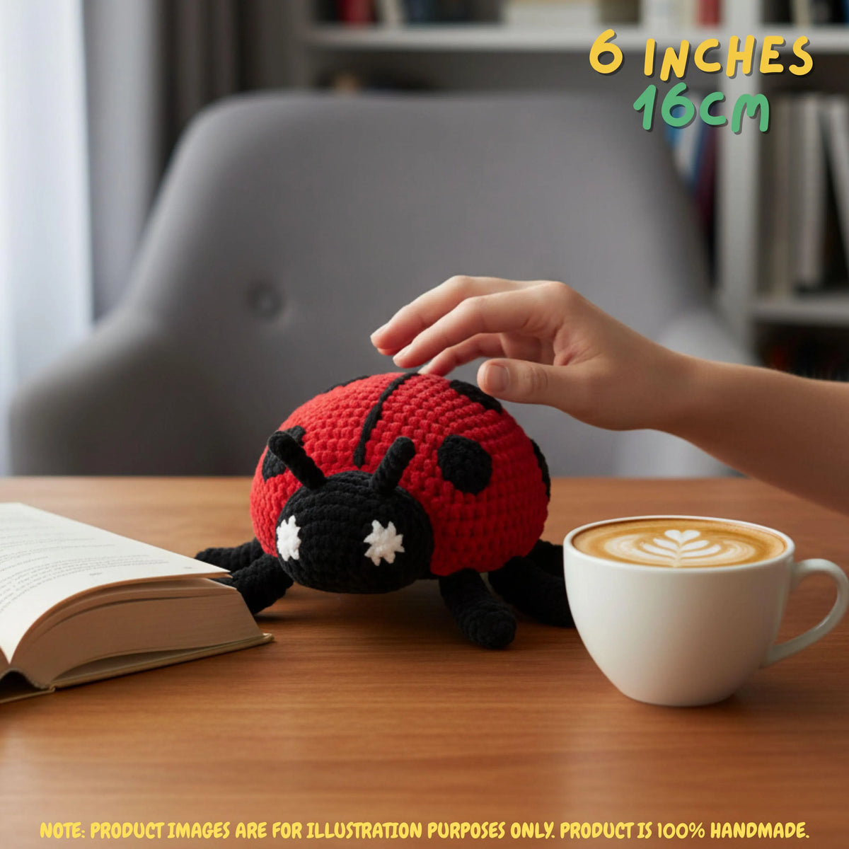 A crocheted ladybug toy sits on a wooden table next to an open book and a cup of latte. A human hand is gently touching the ladybug, and text in the top right reads '6 INCHES 16CM'.