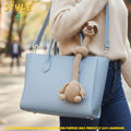 Handmade beige crochet long-neck sloth bag charm with "STYLE 1" text overlay attached to a light blue leather handbag.
