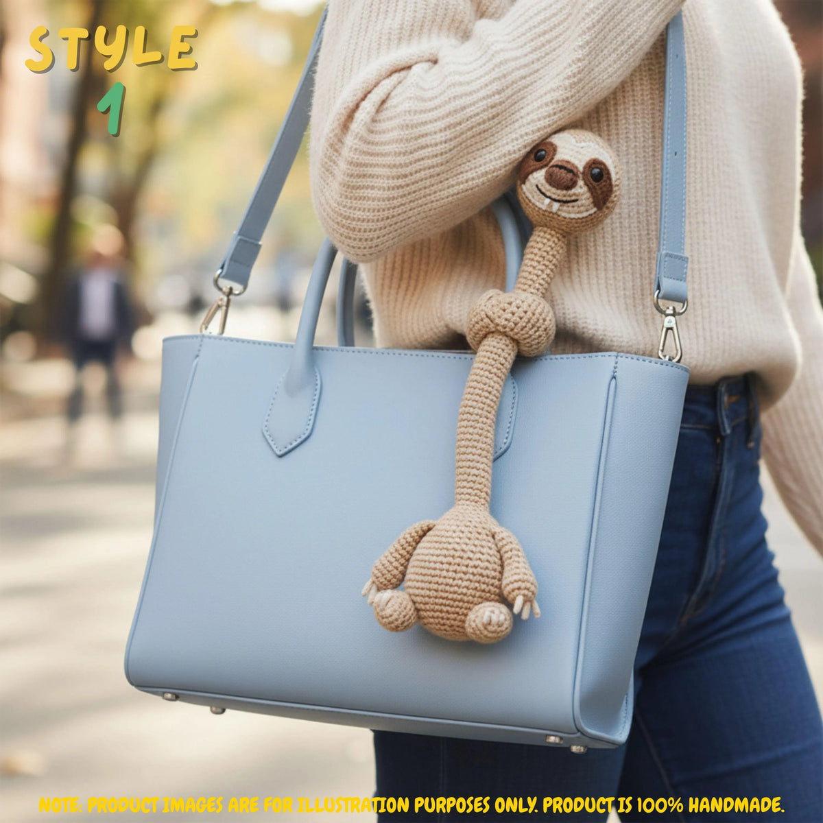 Handmade beige crochet long-neck sloth bag charm with "STYLE 1" text overlay attached to a light blue leather handbag.