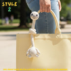 Handmade beige crochet long-neck sloth bag charm with "STYLE 2" text overlay attached to a pastel yellow tote bag.