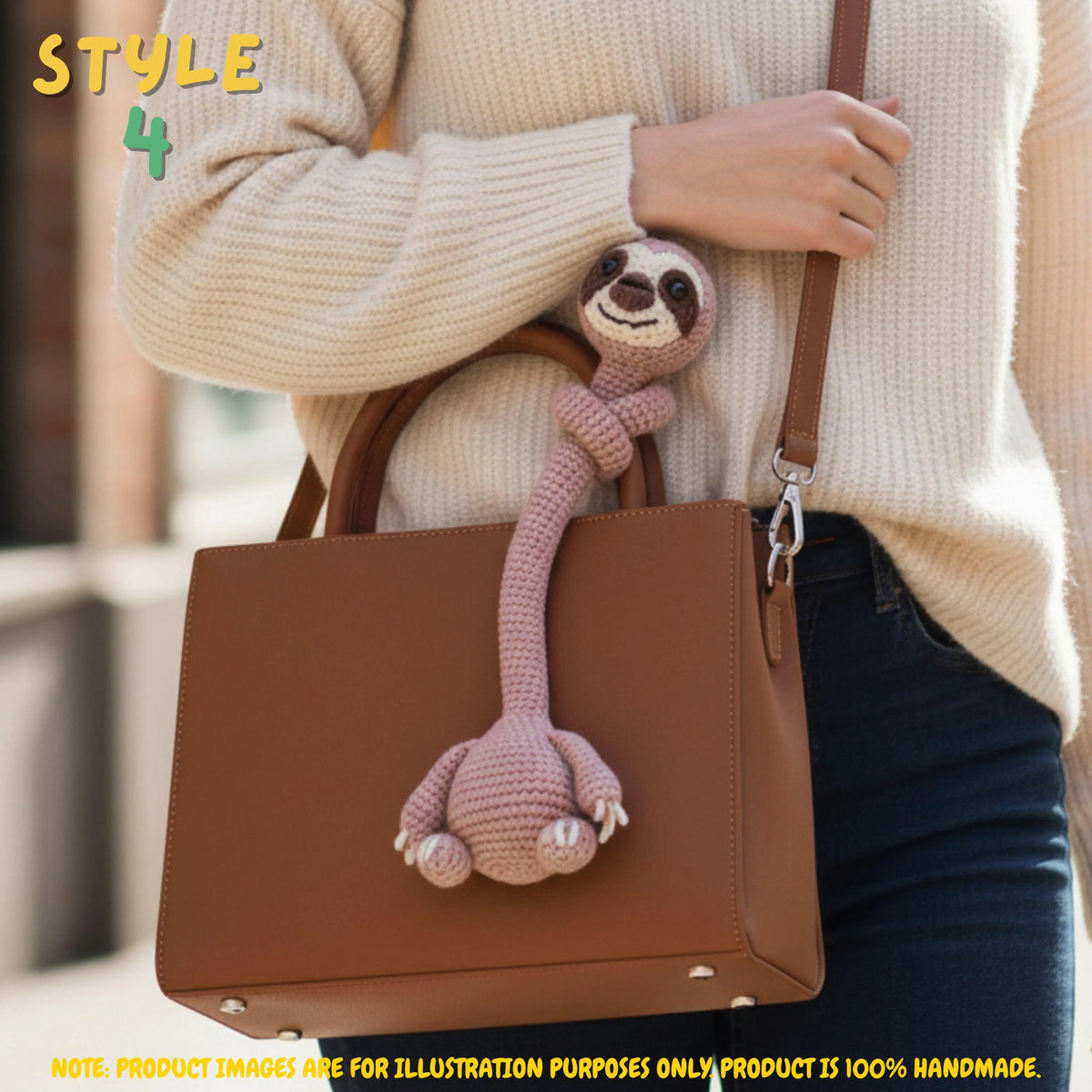 Handmade beige crochet long-neck sloth bag charm with "STYLE 4" text overlay wrapped around the strap of a brown leather shoulder bag worn by a person.