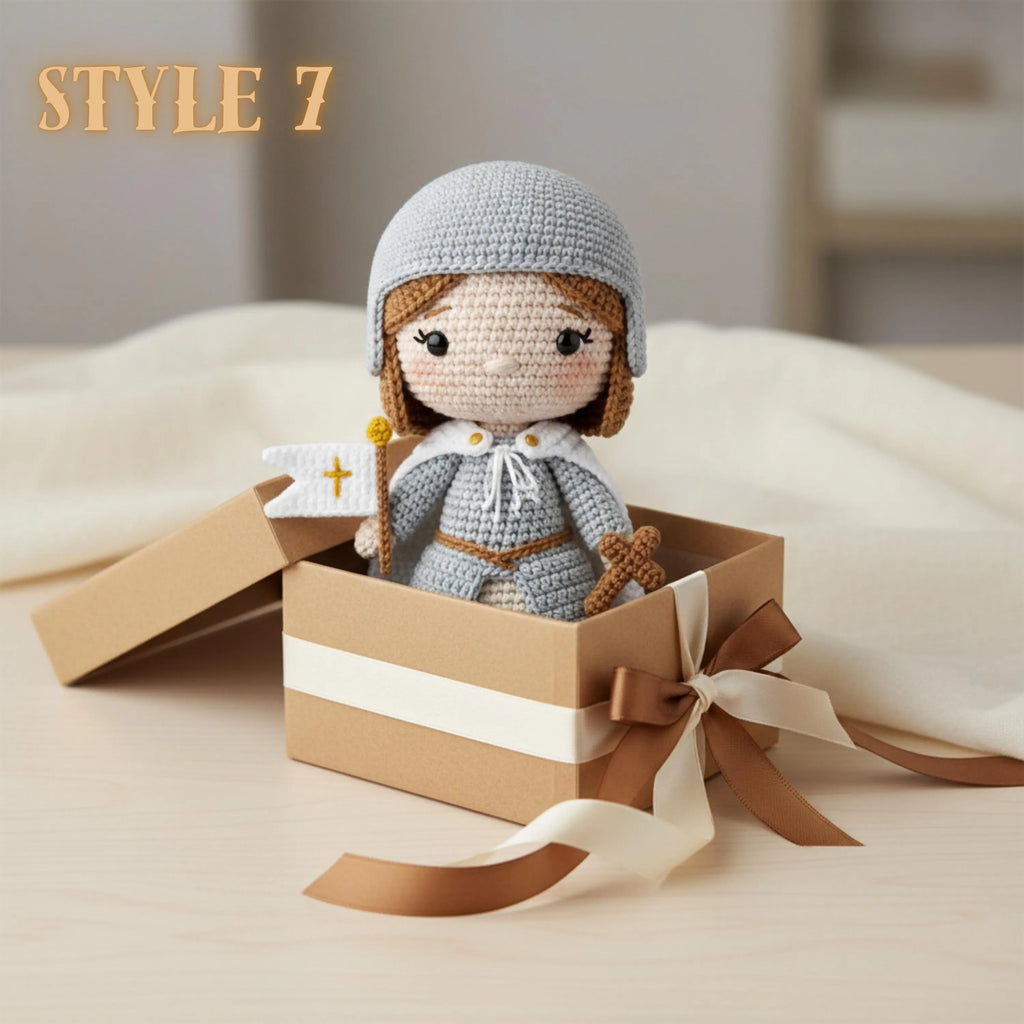 A crocheted doll dressed as a girl in a gray flight helmet and matching gray outfit with brown hair, posed inside a small brown gift box with a cream ribbon. The text 'STYLE 7' appears in the upper left.