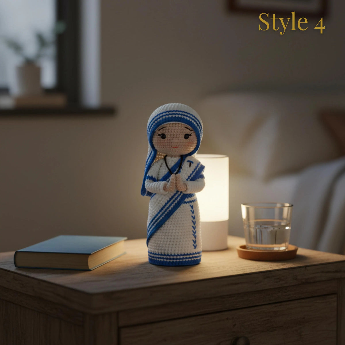 A crocheted female figurine styled on a wooden bedside table next to a lit white lamp, a glass cup, and a book, in a softly blurred bedroom setting. The figurine is white with blue stripes and a black face, and the text 'Style 4' appears in the top right corner.