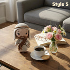 A crocheted doll dressed in a beige and brown robe stands on a wooden coffee table beside a cup of coffee, an open book with glasses, and a small vase of pink flowers. A gray sofa is visible in the background, and the text 'Style 5' appears in the top right.