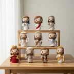 Nine crocheted Jesus figurines in various robes and crowns, displayed on a wooden table and shelf against a light neutral background.