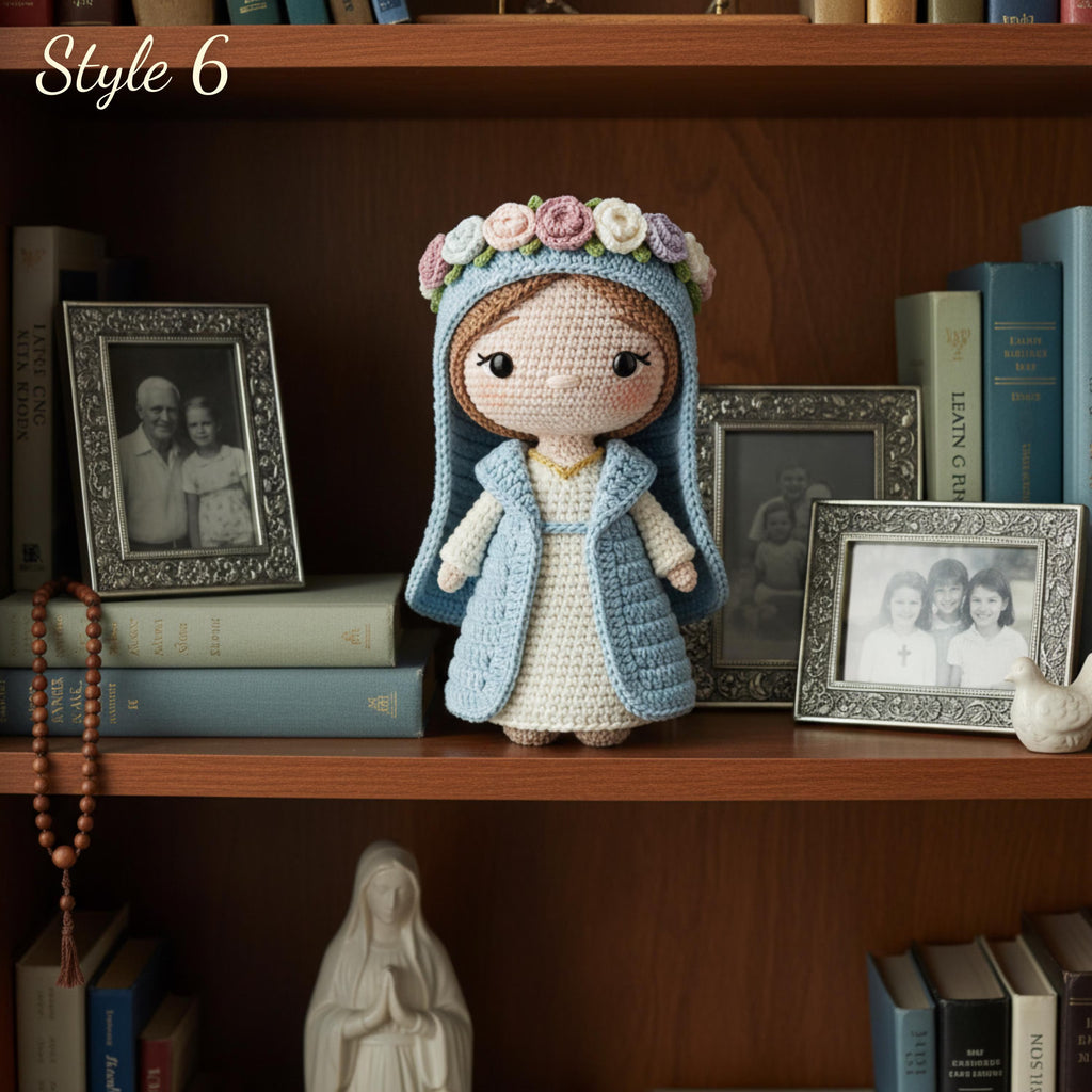 A crocheted doll with a blue hood, cream dress, and pink flower crown stands on a wooden bookshelf surrounded by framed photos, books, and a rosary.