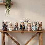 A row of seven small doll-like figurines in varied robes stands on a wooden console table against a warm beige wall, with a hanging green plant and a vase of lavender in the background.