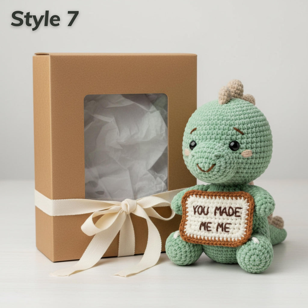 A crocheted green dinosaur plush toy holding a sign that says 'YOU MADE ME ME' sits next to a brown gift box with a cream ribbon, on a light gray background. The text 'Style 7' is in the top-left corner.