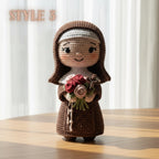 A crocheted doll of a nun in a brown habit holding a bouquet of red, pink, and green flowers, standing on a wooden table with a soft-focus background of white curtains. The text 'STYLE 3' is visible in the top left corner.