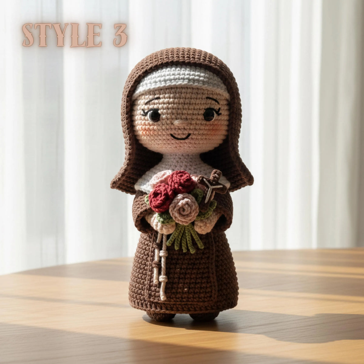 A crocheted doll of a nun in a brown habit holding a bouquet of red, pink, and green flowers, standing on a wooden table with a soft-focus background of white curtains. The text 'STYLE 3' is visible in the top left corner.