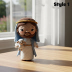 A crocheted doll of Jesus holding a lamb stands on a wooden table in a sunlit room. The doll has brown hair and beard, a white robe, a blue drape, and a gold headband.