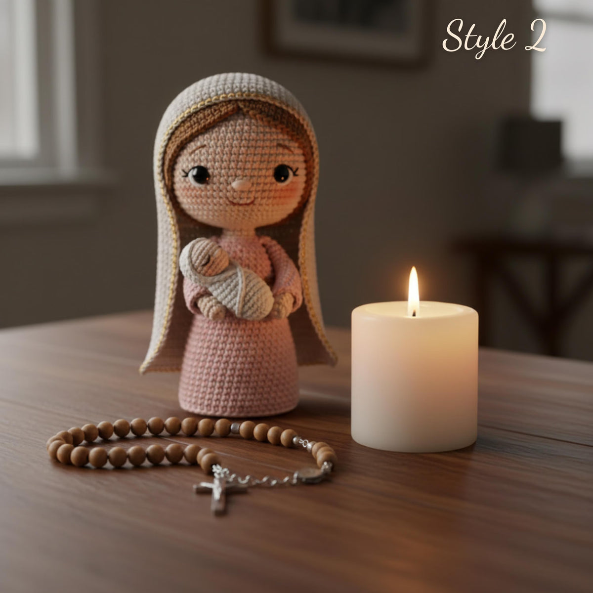 A crocheted doll wearing a beige veil and holding a swaddled baby figure stands on a wooden table beside a lit white candle and a wooden rosary with a silver cross. The background is softly blurred, and the words 'Style 2' appear in the top right.