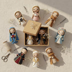 A styled flat-lay of handmade knitted dolls arranged around an open kraft gift box on a textured cream surface. The dolls wear varied garments in beige, blue, red, and brown tones, with some small dried flowers and sewing props like scissors and thread around them.