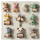 A set of nine crocheted animal plush toys arranged on a light beige fabric background, each holding a small sign with a message. A small bouquet of pink and purple flowers is placed in the center.