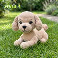 A crocheted plush puppy toy in light beige sits on green grass outdoors, with blurred garden foliage in the background and the text 'STYLE 1' in the upper left corner.